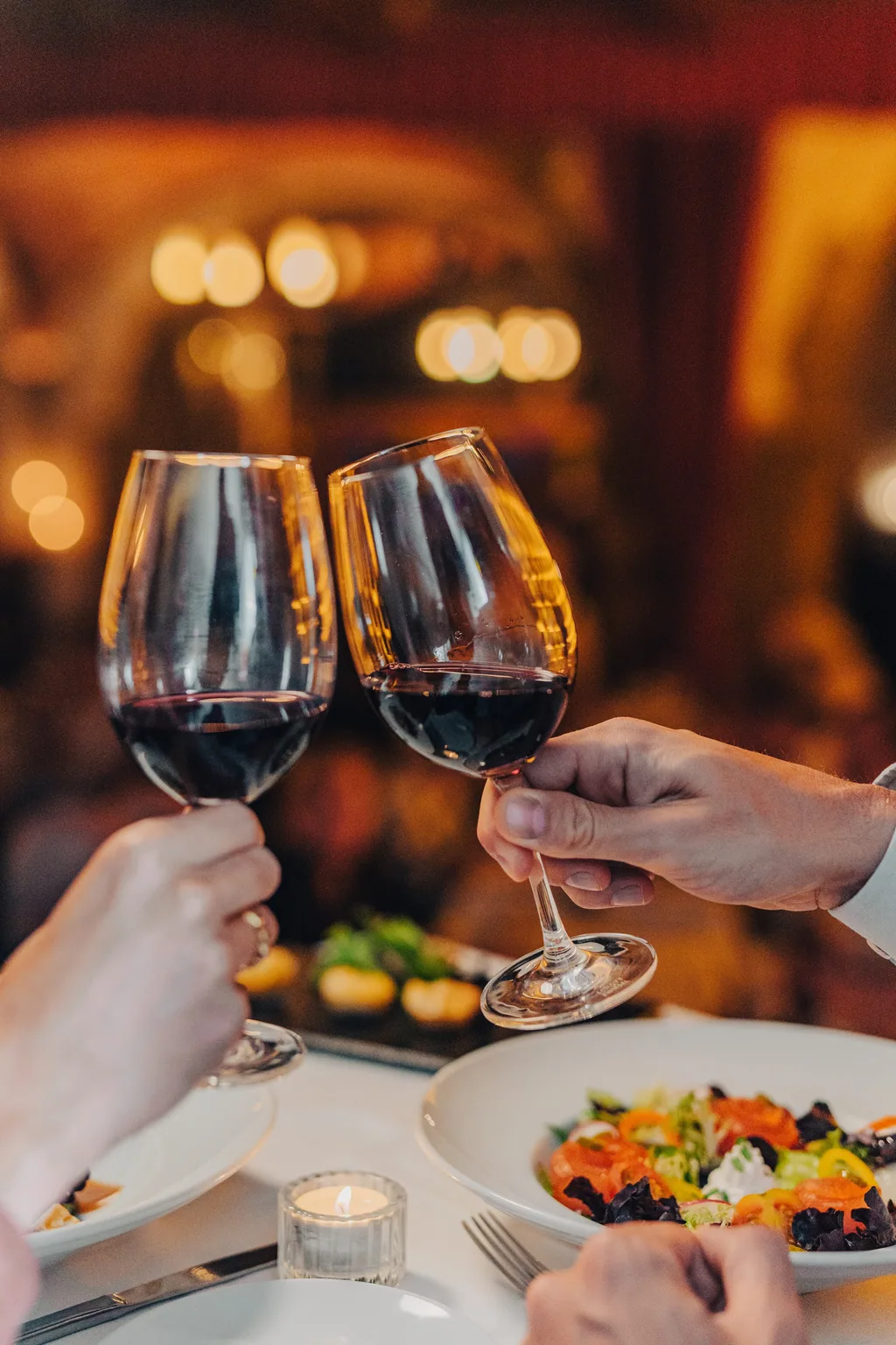 Zwei Gläser Rotwein stoßen über dem Tisch an