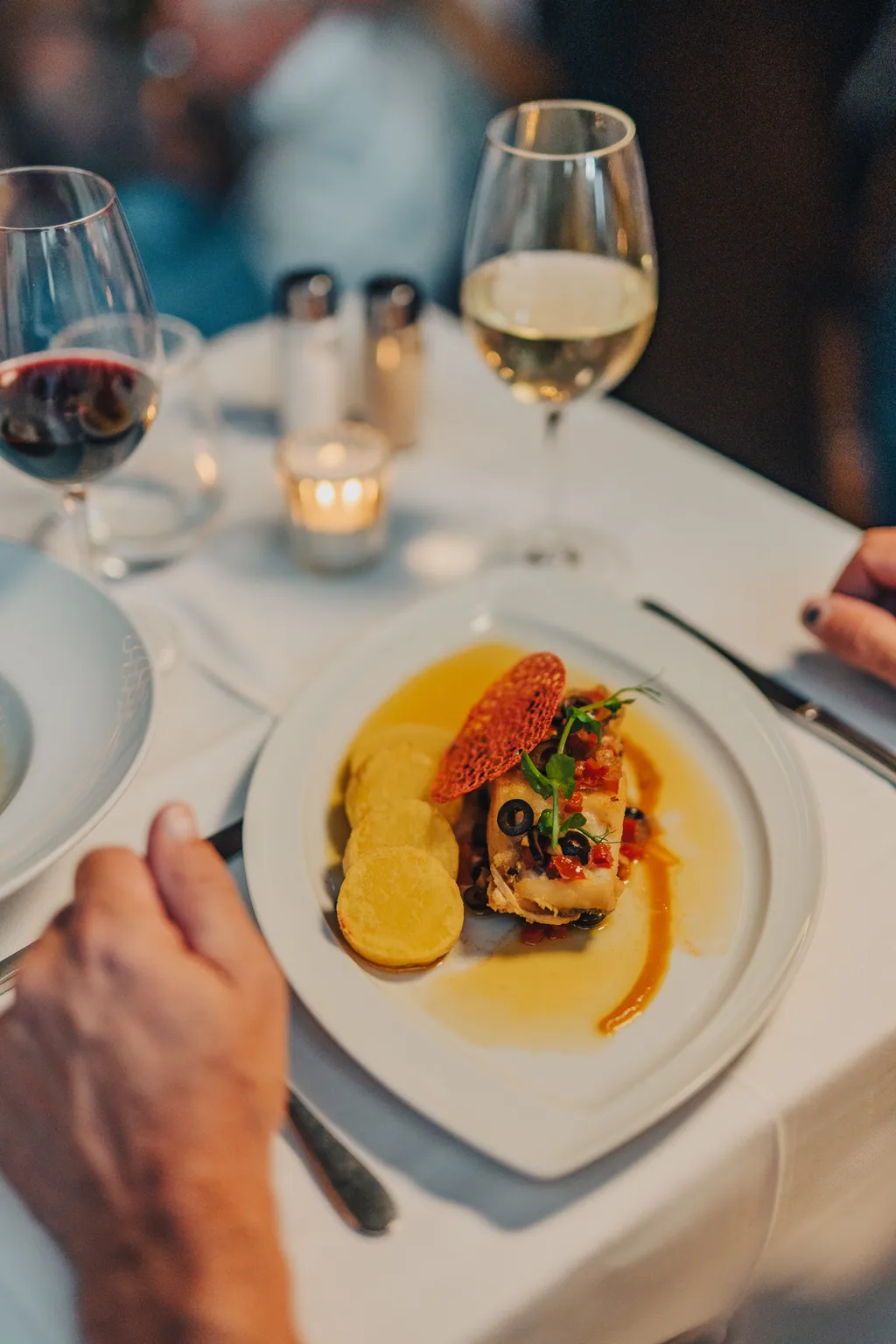 Prato principal servido à mesa, com vinho branco e tinto